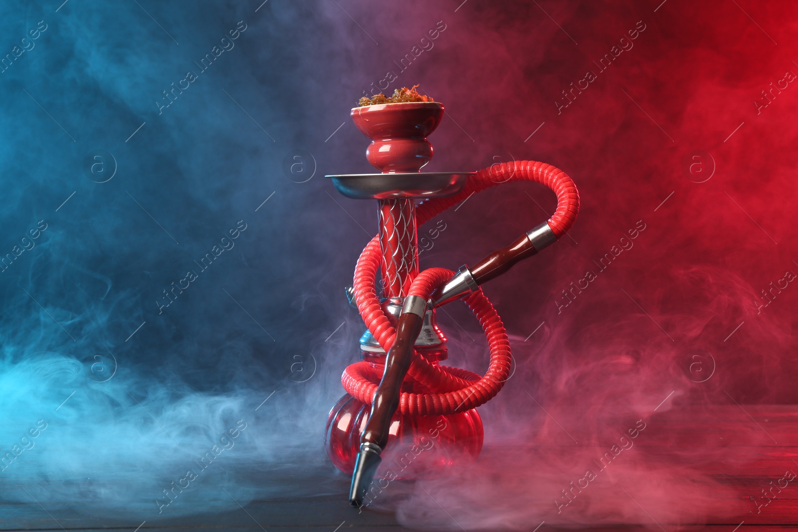 Hookah on wooden table with smoke in color lights against black background Photo of Hookah on wooden table with smoke in color lights against black background