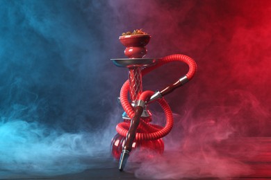 Photo of Hookah on wooden table with smoke in color lights against black background