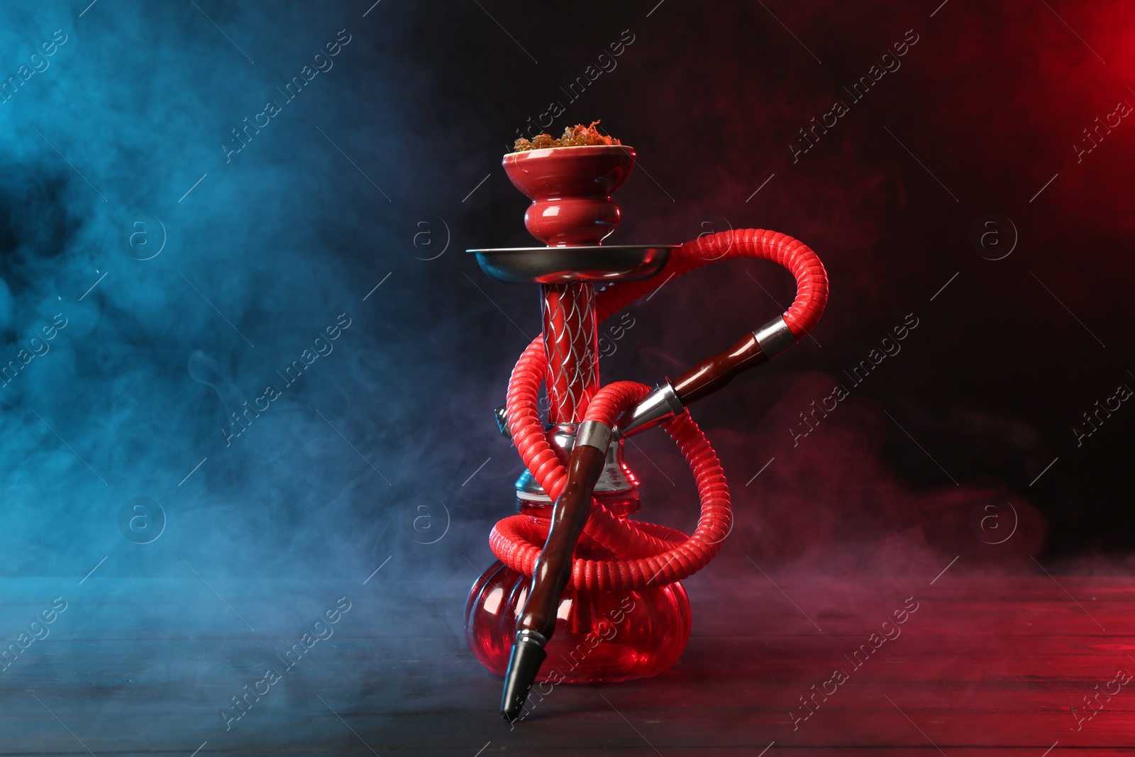 Photo of Hookah on wooden table with smoke in color lights against black background