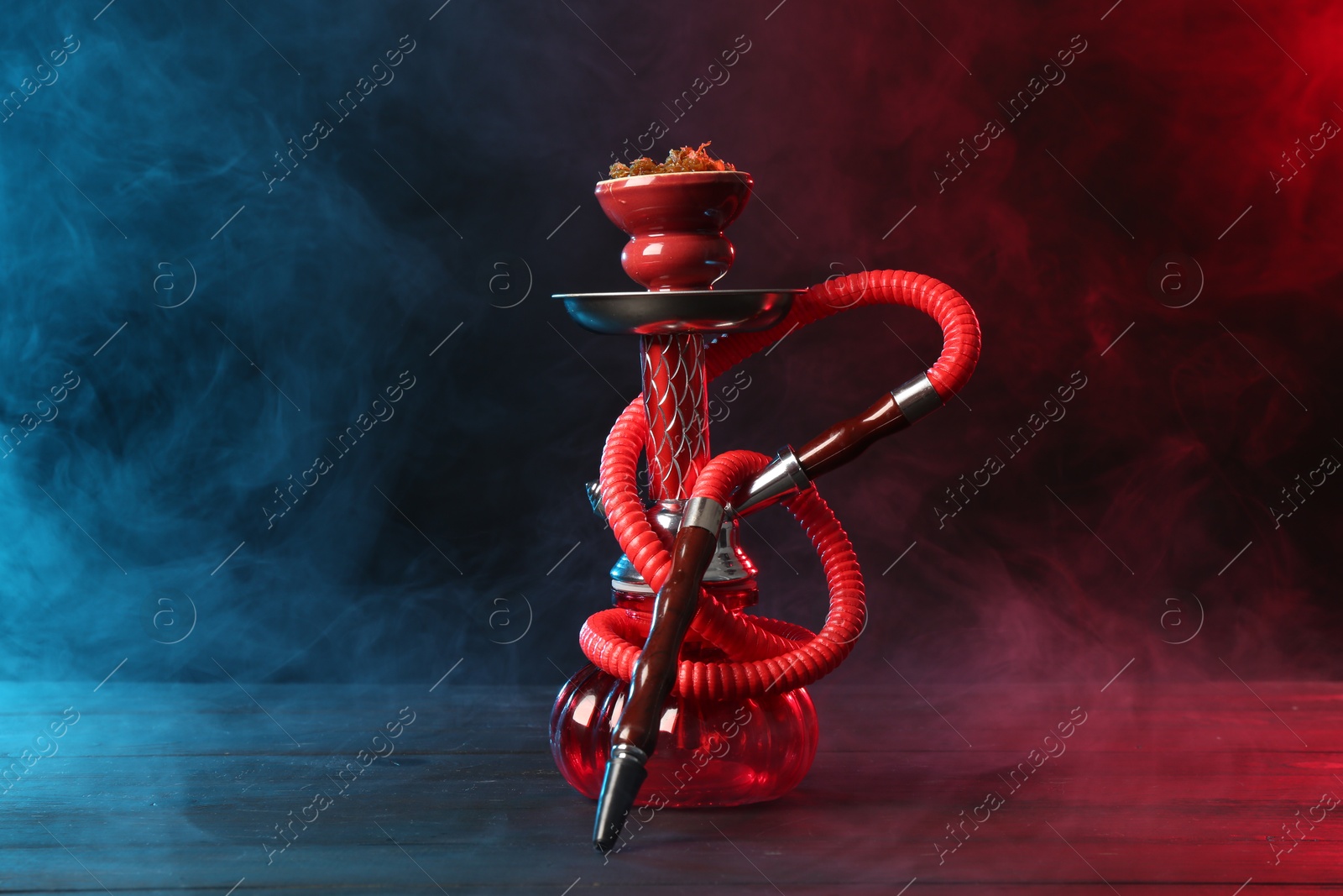 Hookah on wooden table with smoke in color lights against black background Photo of Hookah on wooden table with smoke in color lights against black background