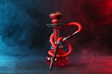 Photo of Hookah on wooden table with smoke in color lights against black background
