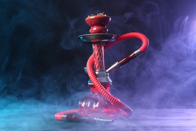 Photo of Hookah on wooden table with smoke in color lights against black background