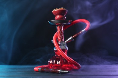 Photo of Hookah on wooden table with smoke in color lights against black background