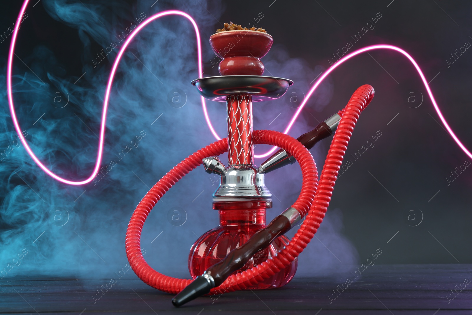 Photo of Hookah on wooden table with smoke in color lights against black background