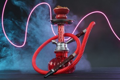 Photo of Hookah on wooden table with smoke in color lights against black background