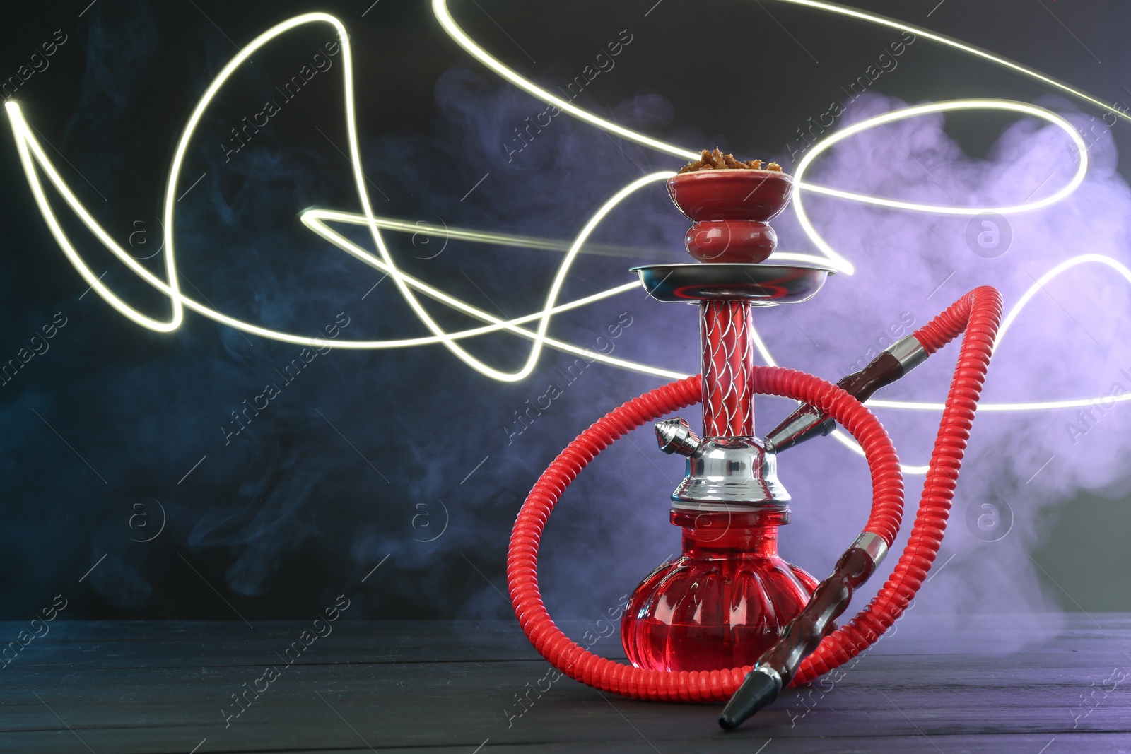 Hookah on wooden table with smoke in color lights against black background Photo of Hookah on wooden table with smoke in color lights against black background
