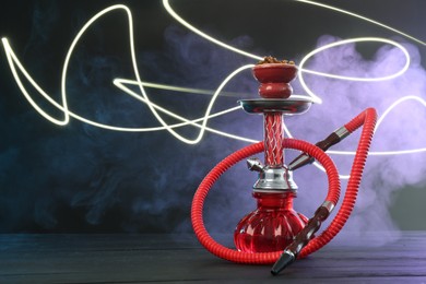 Photo of Hookah on wooden table with smoke in color lights against black background