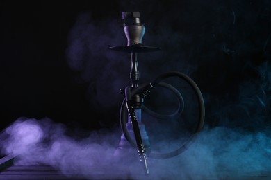 Photo of Hookah on wooden table with smoke in color lights against black background