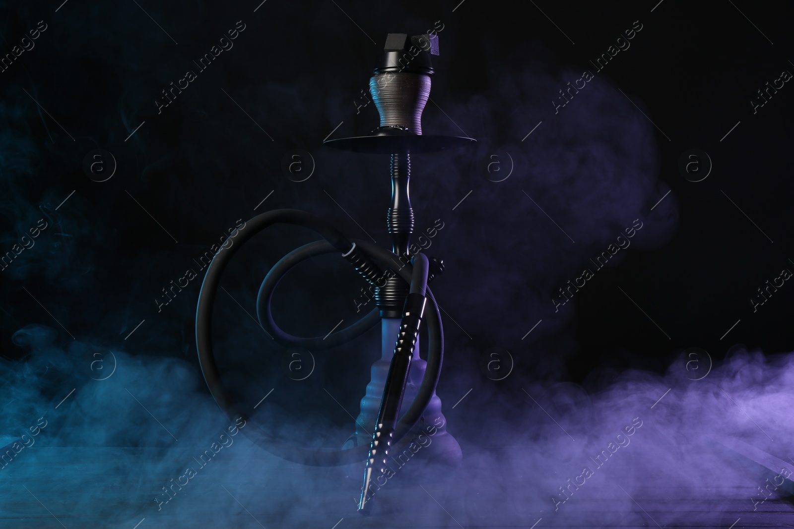 Photo of Hookah on wooden table with smoke in color lights against black background