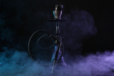 Photo of Hookah on wooden table with smoke in color lights against black background