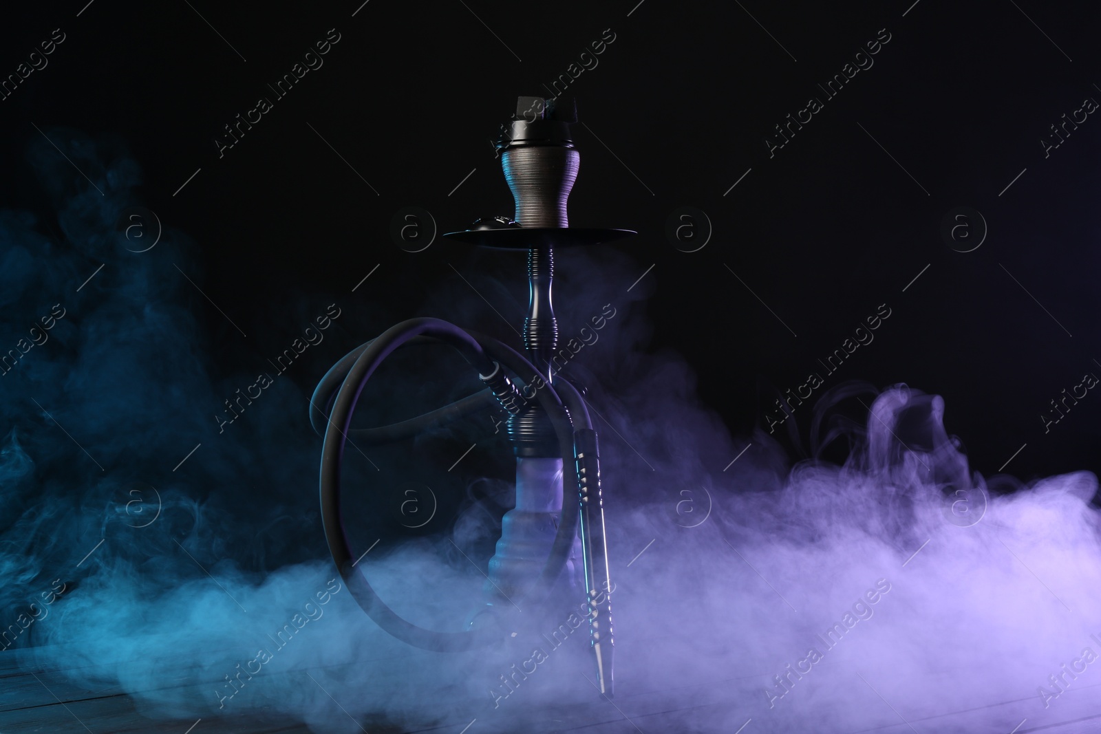 Photo of Hookah on wooden table with smoke in color lights against black background