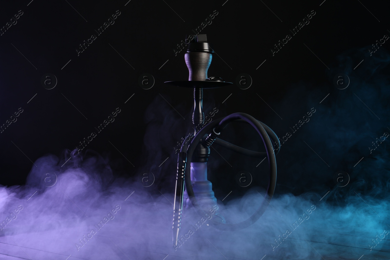 Photo of Hookah on wooden table with smoke in color lights against black background