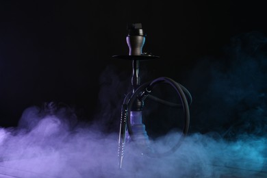 Photo of Hookah on wooden table with smoke in color lights against black background