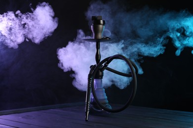 Photo of Hookah on wooden table with smoke in color lights against black background