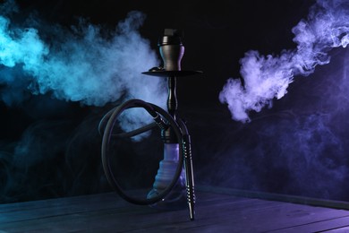 Photo of Hookah on wooden table with smoke in color lights against black background
