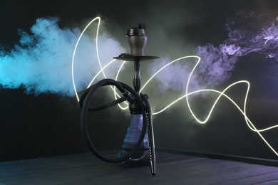 Photo of Hookah on wooden table with smoke in color lights against black background