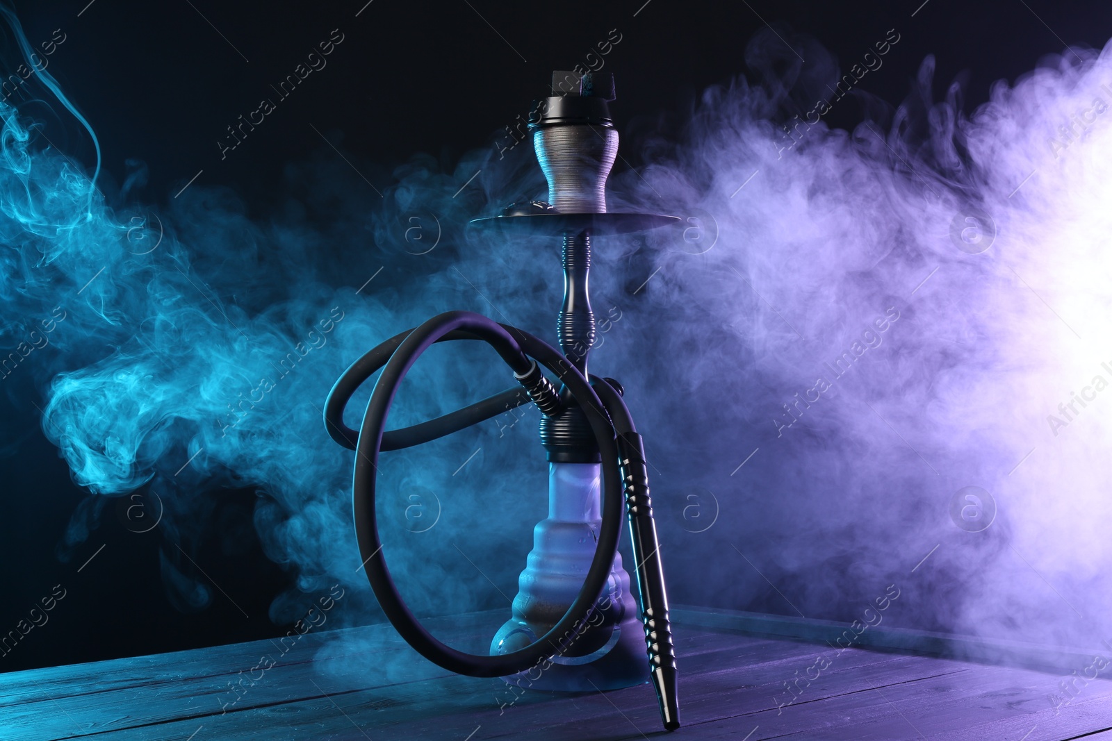 Hookah on wooden table with smoke in color lights against black background Photo of Hookah on wooden table with smoke in color lights against black background