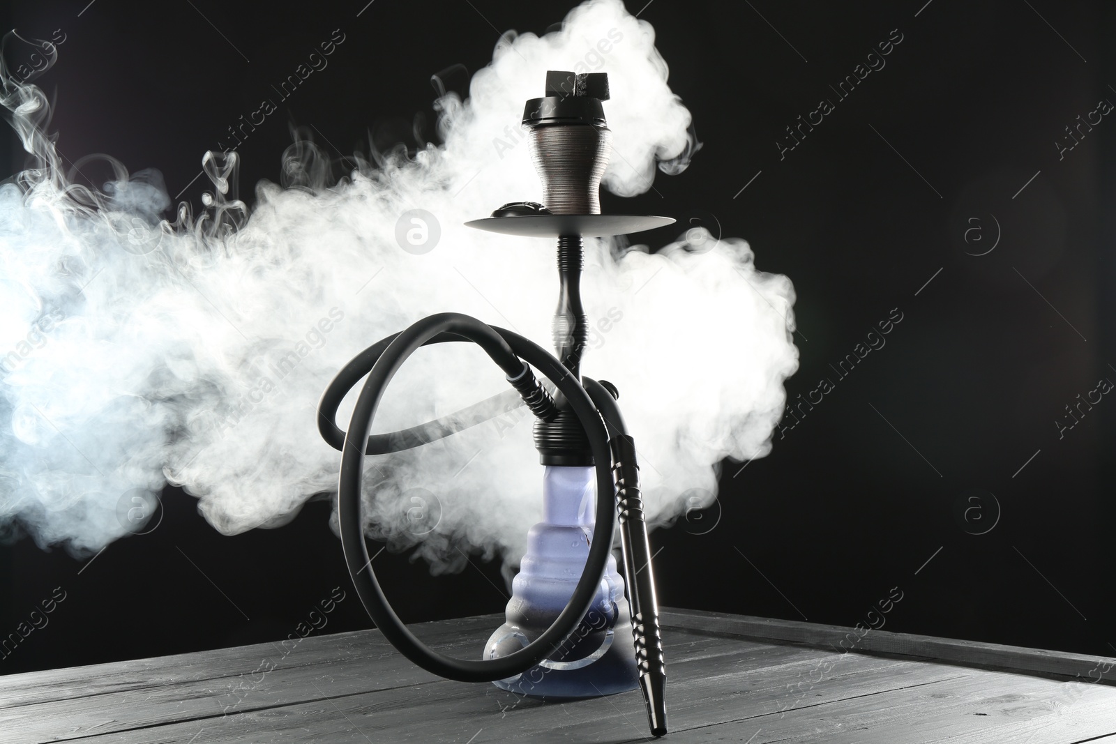 Photo of Hookah on wooden table with smoke against black background