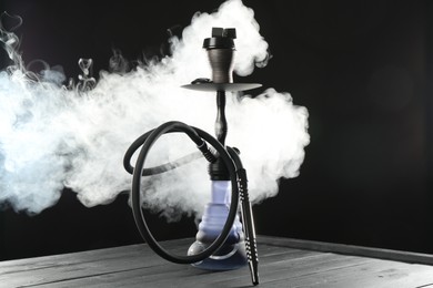 Photo of Hookah on wooden table with smoke against black background