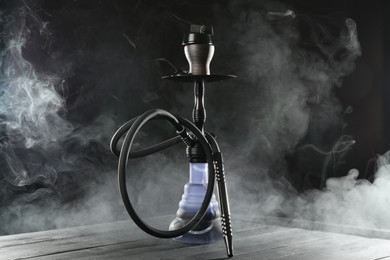 Photo of Hookah on wooden table with smoke against black background