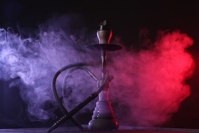 Photo of Hookah on wooden table with smoke in color lights against black background