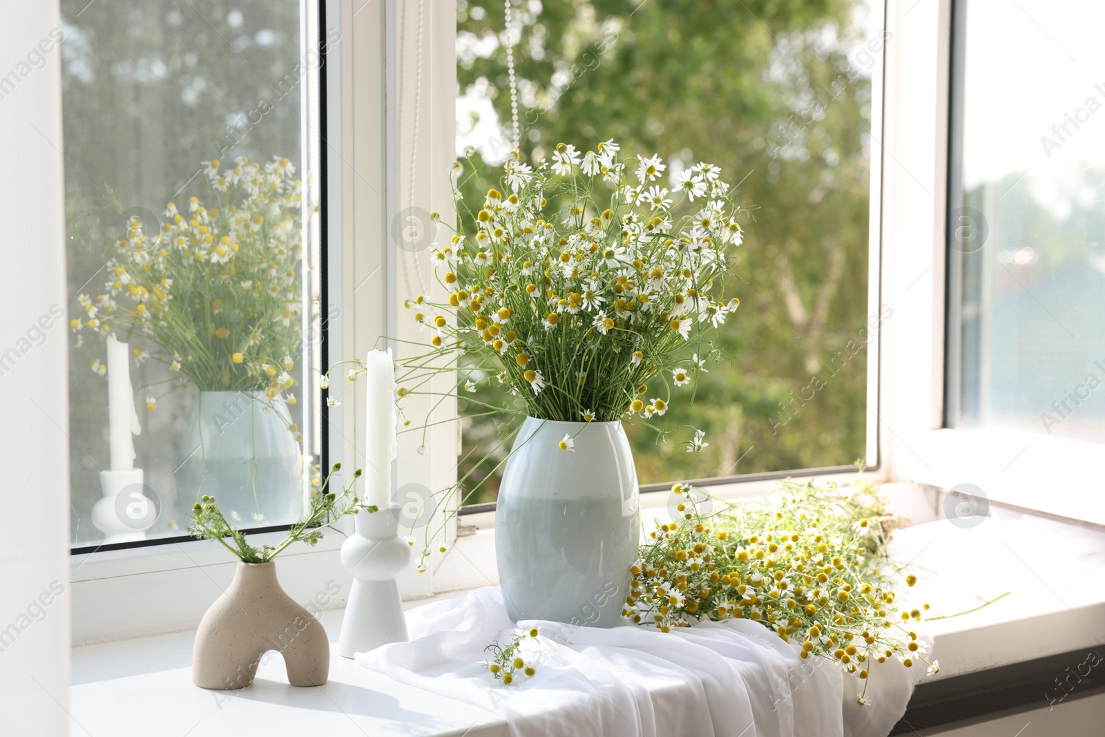 Beautiful chamomile flowers and candle on window sill indoors Photo of Beautiful chamomile flowers and candle on window sill indoors