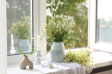 Photo of Beautiful chamomile flowers and candle on window sill indoors