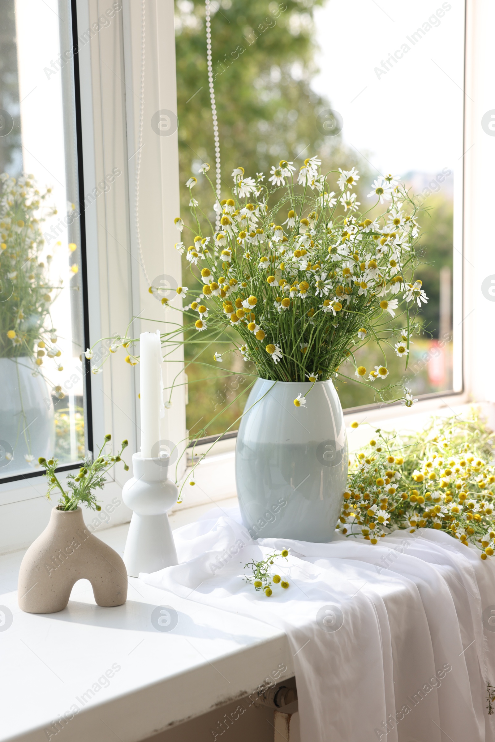 Beautiful chamomile flowers and candle on window sill indoors Photo of Beautiful chamomile flowers and candle on window sill indoors