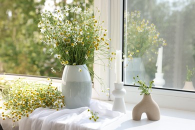 Photo of Beautiful chamomile flowers and candle on window sill indoors