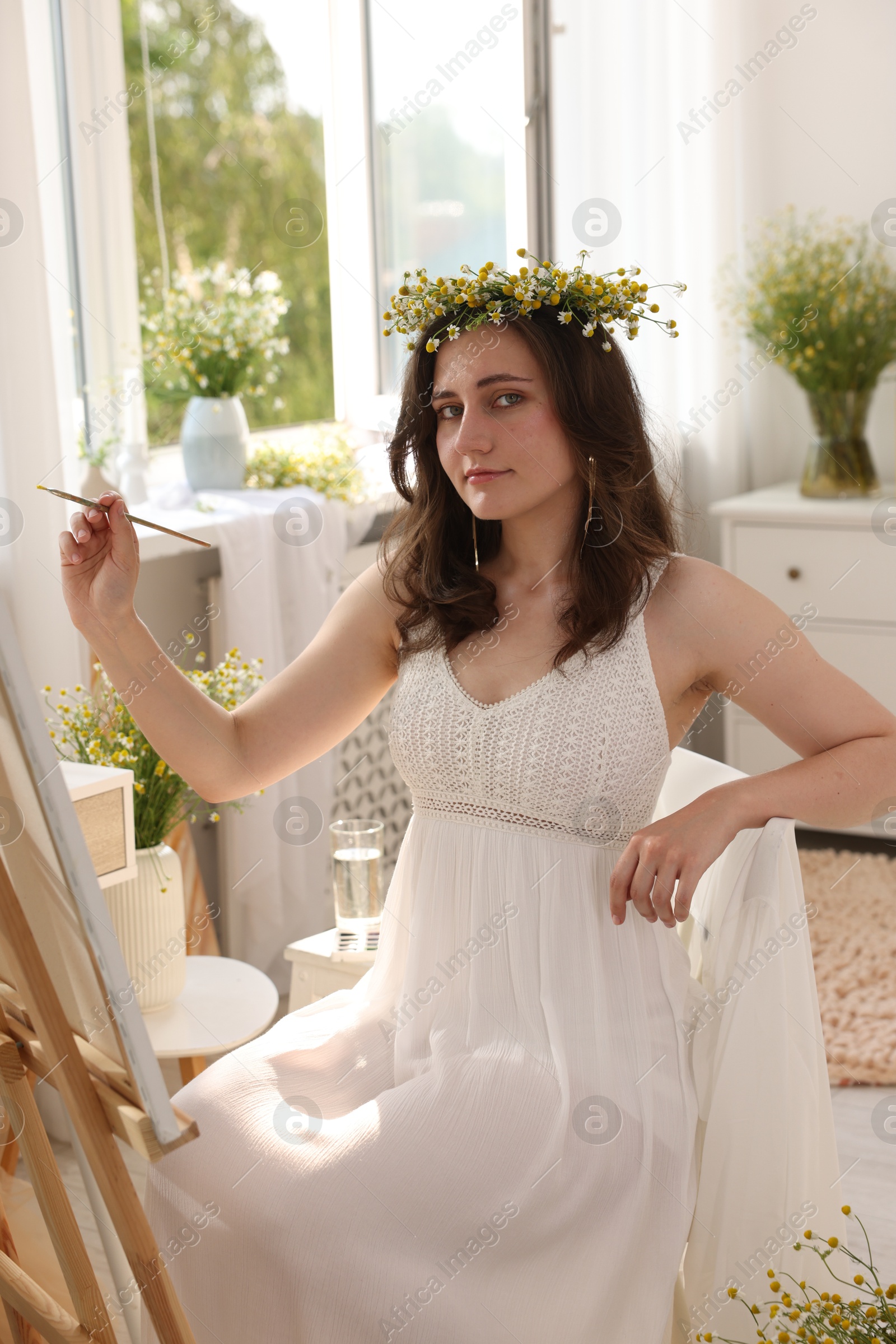 Beautiful woman with chamomile wreath drawing on canvas indoors Photo of Beautiful woman with chamomile wreath drawing on canvas indoors