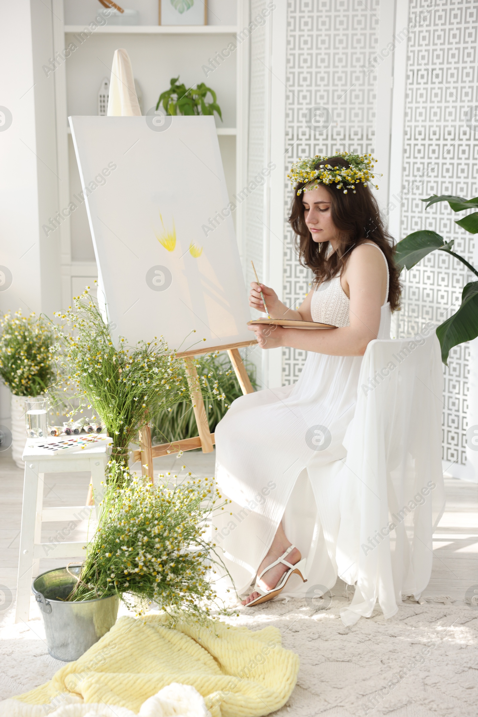 Beautiful woman with chamomile wreath drawing on canvas indoors Photo of Beautiful woman with chamomile wreath drawing on canvas indoors