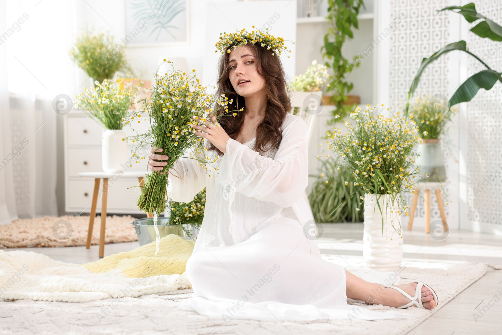 Beautiful woman with chamomile flowers on floor indoors Photo of Beautiful woman with chamomile flowers on floor indoors