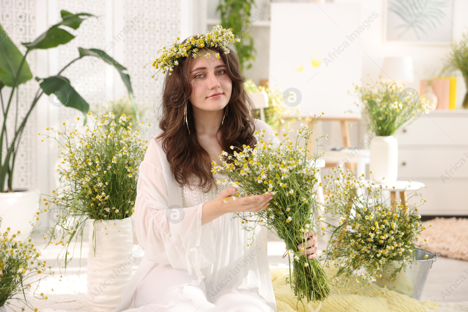 Beautiful woman with chamomile flowers on floor indoors Photo of Beautiful woman with chamomile flowers on floor indoors