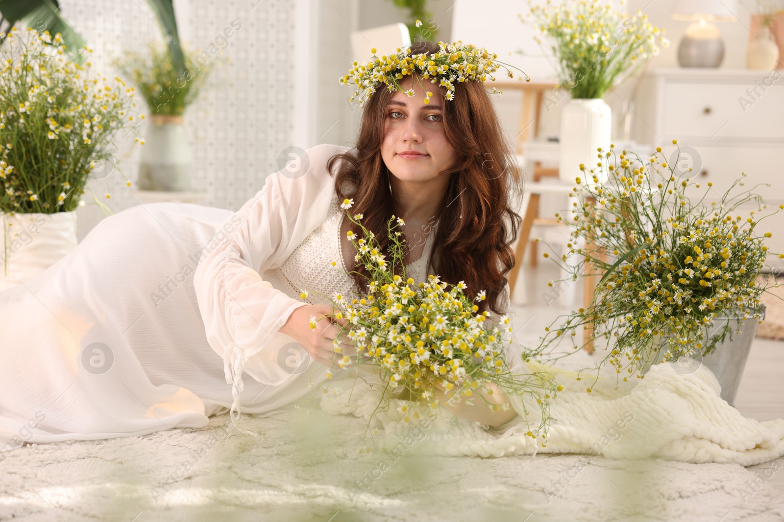 Beautiful woman with chamomile flowers on floor indoors Photo of Beautiful woman with chamomile flowers on floor indoors