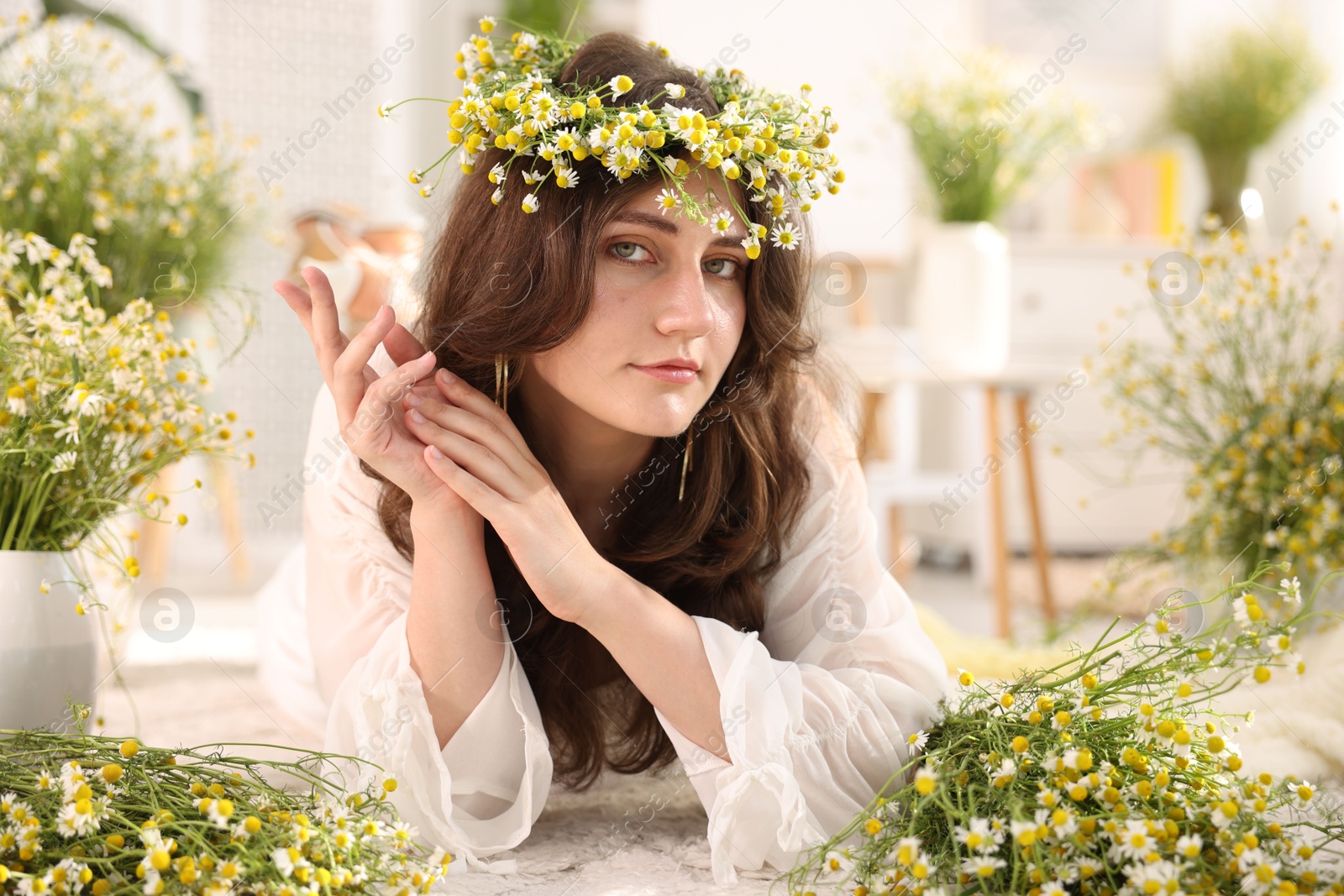 Beautiful woman with chamomile flowers on floor indoors Photo of Beautiful woman with chamomile flowers on floor indoors