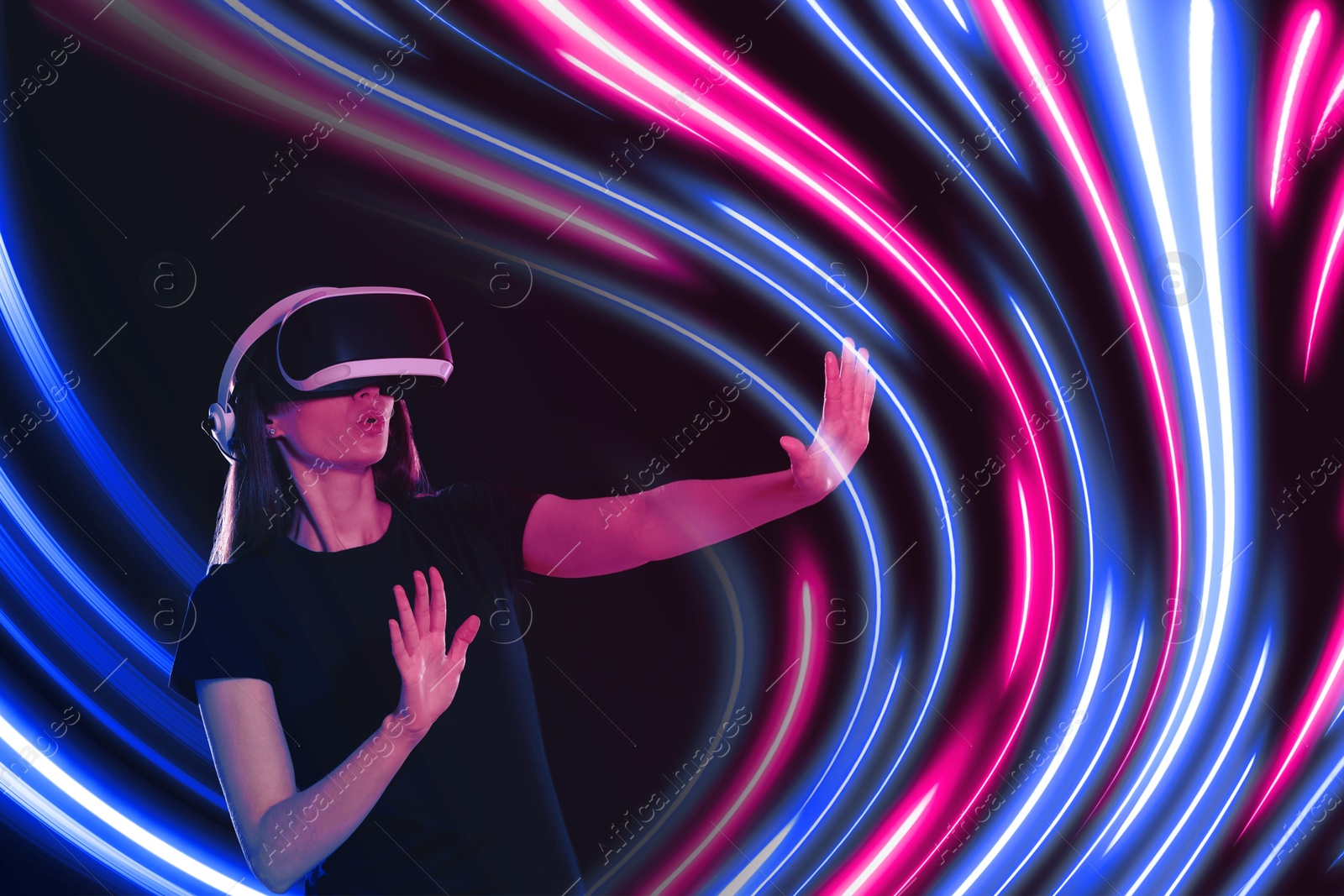 Woman using virtual reality headset on dark background. Bright neon lines around her Image of Woman using virtual reality headset on dark background. Bright neon lines around her