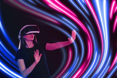 Image of Woman using virtual reality headset on dark background. Bright neon lines around her