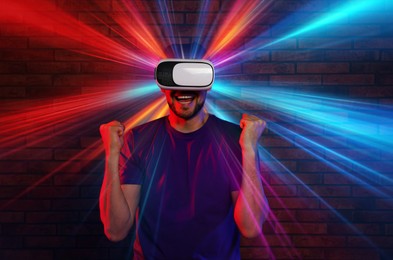 Image of Man using virtual reality headset against brick wall. Bright neon lights coming out of device
