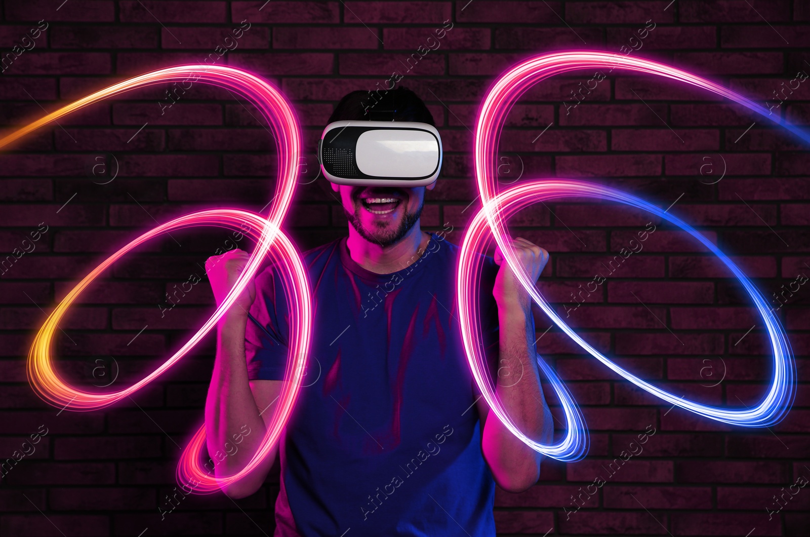 Man using virtual reality headset against brick wall. Bright neon lines around him Image of Man using virtual reality headset against brick wall. Bright neon lines around him