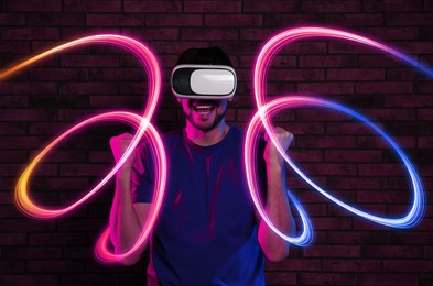 Image of Man using virtual reality headset against brick wall. Bright neon lines around him
