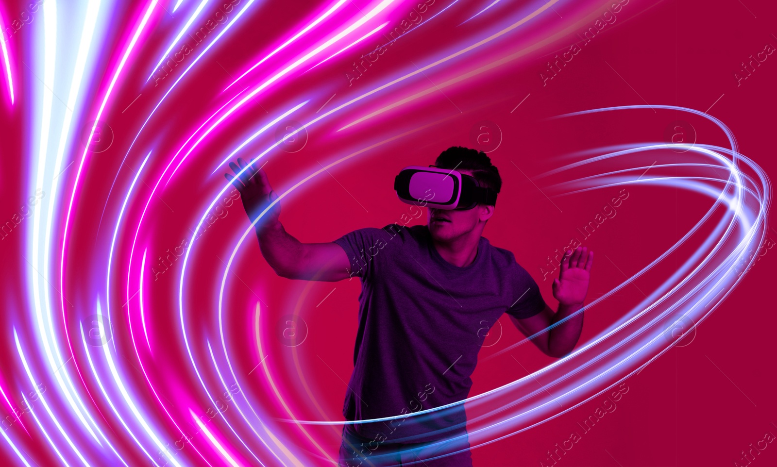 Man using virtual reality headset on crimson color background. Bright neon lines around him Image of Man using virtual reality headset on crimson color background. Bright neon lines around him