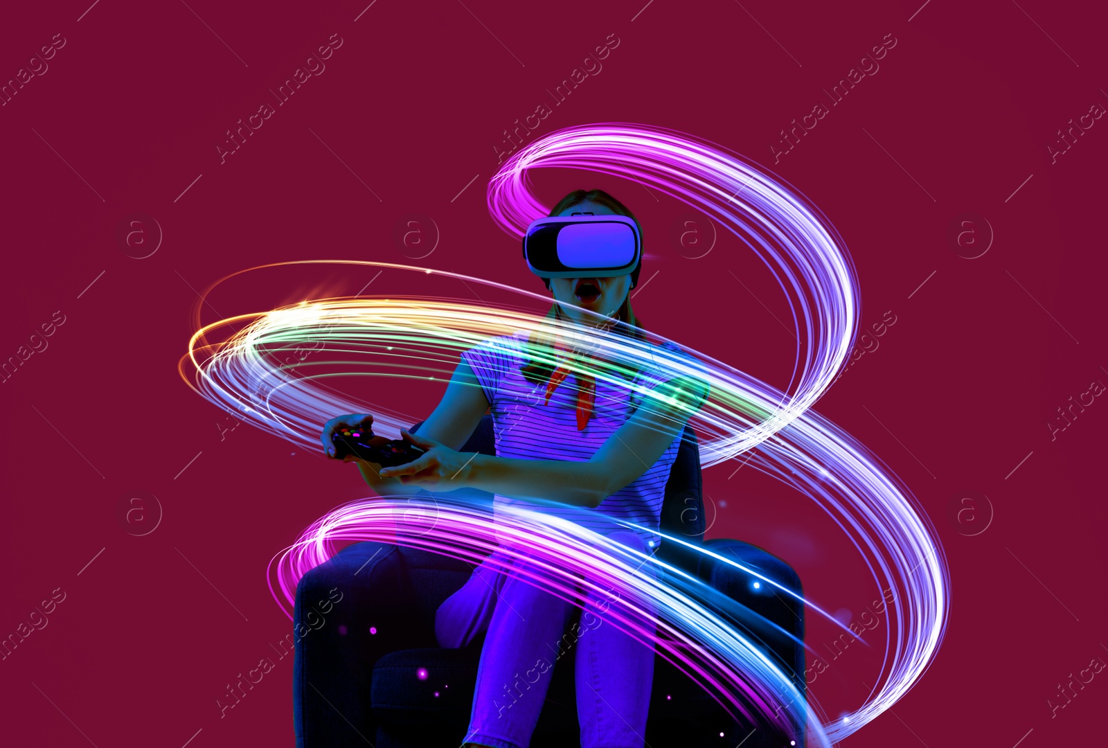 Woman using virtual reality headset and controller in armchair on crimson color background. Bright neon lines around her Image of Woman using virtual reality headset and controller in armchair on crimson color background. Bright neon lines around her