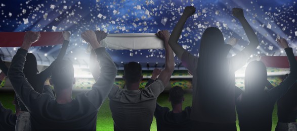 Image of Excited fans celebrating victory in spectator area under falling confetti at stadium, back view