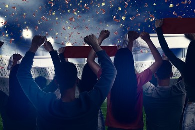 Image of Excited fans celebrating victory in spectator area under falling confetti at stadium, back view