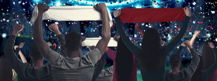 Image of Excited fans celebrating victory in spectator area under falling confetti at stadium, back view