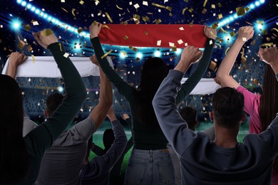 Image of Excited fans celebrating victory in spectator area under falling confetti at stadium, back view