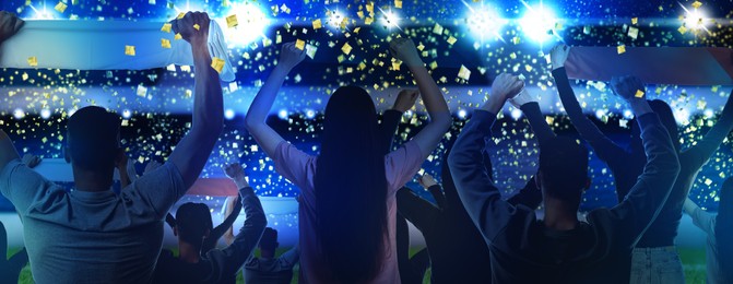 Image of Excited fans celebrating victory in spectator area under falling confetti at stadium, back view