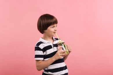 Photo of Cute little boy drinking lemonade on pink background. Refreshing drink