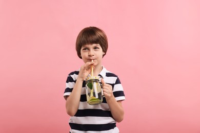 Photo of Cute little boy drinking lemonade on pink background. Refreshing drink
