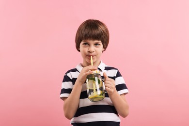 Photo of Cute little boy drinking lemonade on pink background. Refreshing drink